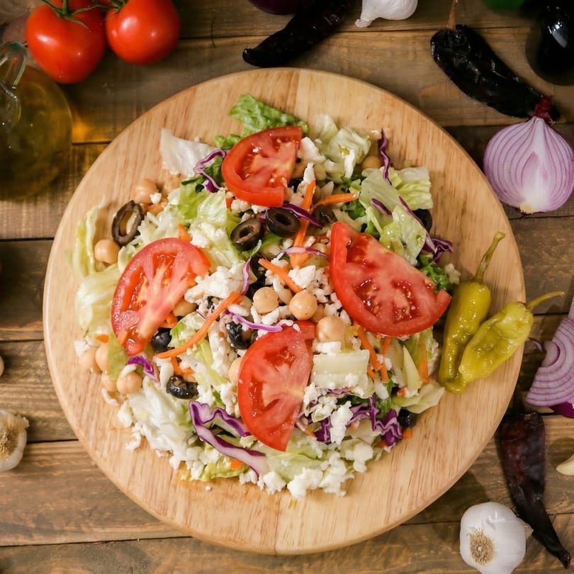 A vibrant salad with lettuce, tomatoes, olives, chickpeas, and feta cheese on a wooden board.